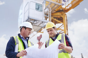 Bauarbeiter und Ingenieur bei der Überprüfung von Bauplänen unter einem Kran auf einer Baustelle - CAIF11604