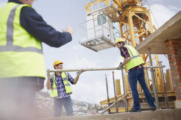 Bauarbeiter heben einen Metallmast unter einem Kran auf einer Baustelle an - CAIF11608