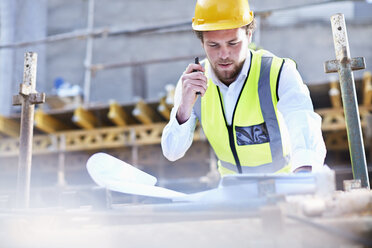 Engineer with blueprints and walkie-talkie working at construction site - CAIF11612