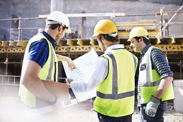 Construction workers and engineer reviewing blueprints at construction site - CAIF11614