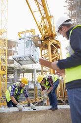 Bauarbeiter beim Einsatz eines Nivelliergeräts unter einem Kran auf einer Baustelle - CAIF11615