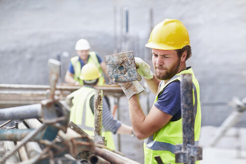 Bauarbeiter trägt Metallstange auf Baustelle - CAIF11618