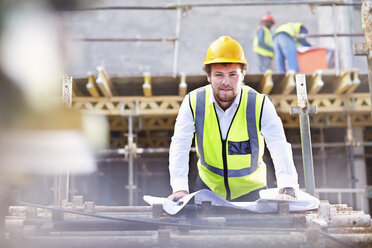 Portrait confident engineer with blueprints at construction site - CAIF11620