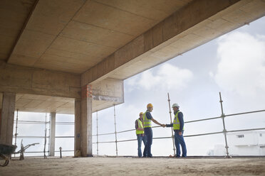 Construction workers handshaking at highrise construction site - CAIF11622