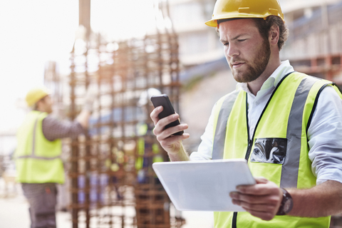 Construction worker with digital tablet texting with cell phone at construction site stock photo