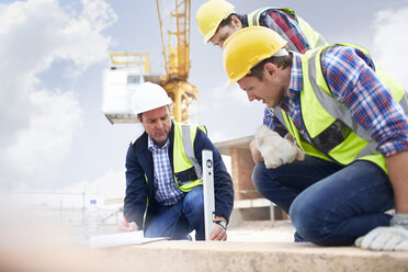 Construction workers and engineer using level tool at construction site - CAIF11629