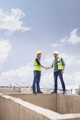 Construction workers handshaking at highrise construction site - CAIF11632