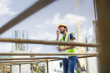 Engineer with blueprints using walkie-talkie at construction site - CAIF11638