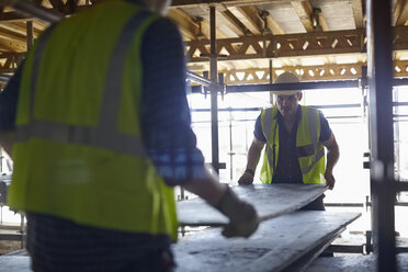 Bauarbeiter heben Sperrholzplatten auf der Baustelle - CAIF11639