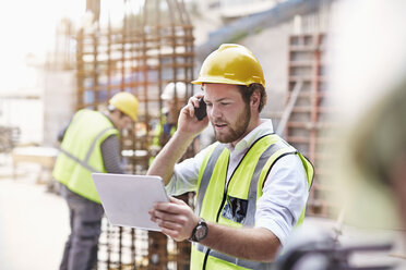 Ingenieur mit digitalem Tablet, der auf einer Baustelle mit einem Handy telefoniert - CAIF11640