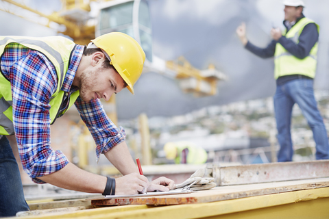 Bauarbeiter schreibt auf einer Baustelle auf einem Klemmbrett, lizenzfreies Stockfoto