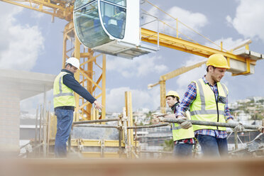 Foreman guiding construction workers below crane at construction site - CAIF11643