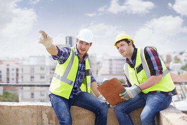 Bauarbeiter und Ingenieur mit Klemmbrett, die auf eine Hochhausbaustelle zeigen - CAIF11647