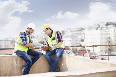 Bauarbeiter und Ingenieur mit Klemmbrett im Gespräch auf einer Hochhausbaustelle - CAIF11649