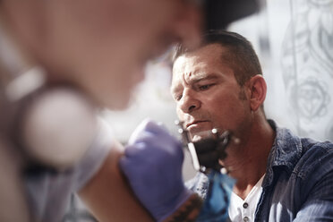 Focused tattoo artist tattooing man’s arm - CAIF11660