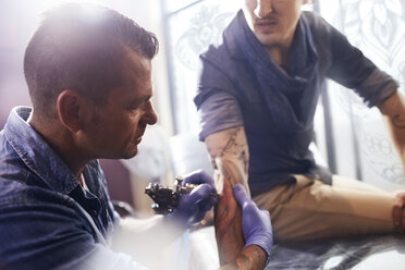 Tattoo artist tattooing man’s forearm - CAIF11665