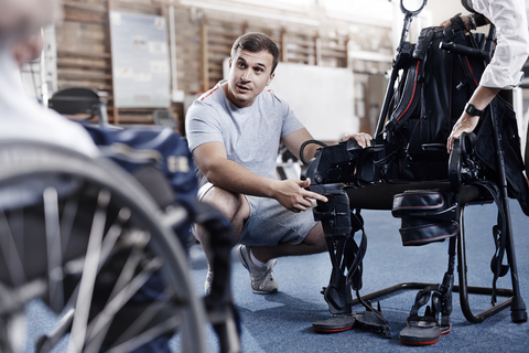 Ein Physiotherapeut erklärt einem Mann im Rollstuhl seine Ausrüstung, lizenzfreies Stockfoto