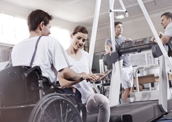 Physiotherapeut zeigt einem Mann im Rollstuhl ein digitales Tablet - CAIF11677
