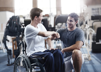 Physical therapist fist bumping man in wheelchair - CAIF11684