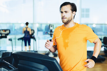 Schwitzender Mann mit Kopfhörern beim Laufen auf dem Laufband im Fitnessstudio - CAIF11699