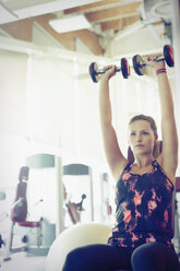 Konzentrierte Frau beim Schulterdrücken mit Kurzhanteln im Fitnessstudio - CAIF11708