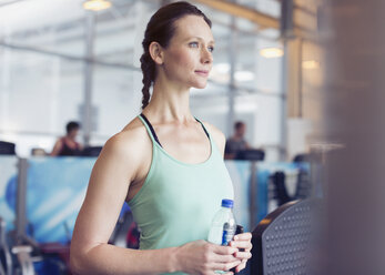 Nachdenkliche Frau trinkt Wasser im Fitnessstudio - CAIF11721