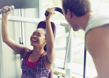 Personal Trainer ermutigt Frau bei der Benutzung von Trainingsgeräten im Fitnessstudio - CAIF11732