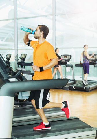 Mann trinkt Wasser und läuft auf dem Laufband im Fitnessstudio, lizenzfreies Stockfoto