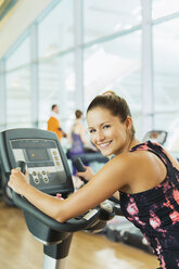 Portrait smiling woman on exercise bike at gym - CAIF11743