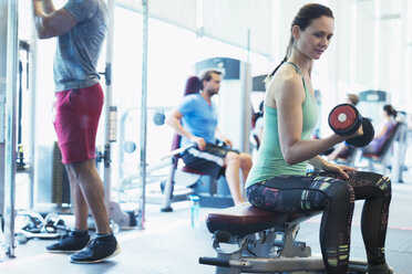 Frau macht Bizeps-Curls mit Kurzhanteln im Fitnessstudio - CAIF11747