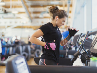 Frau läuft auf dem Laufband im Fitnessstudio mit Kopfhörern - CAIF11751