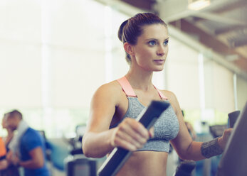 Konzentrierte Frau beim Training auf dem Ellipsentrainer im Fitnessstudio - CAIF11765