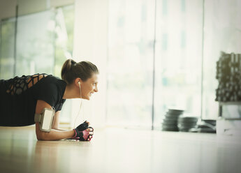 Lächelnde Frau in Plankenstellung auf dem Boden eines Fitnessstudios - CAIF11784