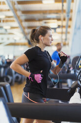 Focused woman running on treadmill at gym - CAIF11787
