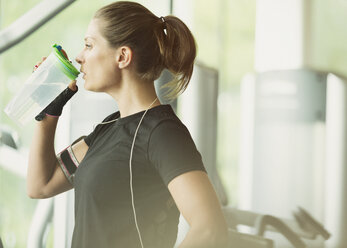 Frau ruht sich aus und trinkt Wasser im Fitnessstudio - CAIF11791