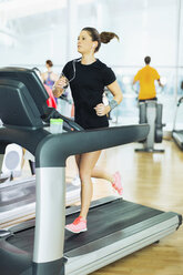 Woman running on treadmill with headphones at gym - CAIF11795