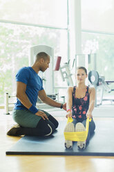 Personal Trainer führt Frau Stretching Beine mit Widerstand Band im Fitnessstudio - CAIF11805