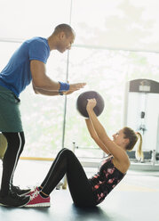 Personal Trainer führt Frau mit Medizinball im Fitnessstudio - CAIF11819