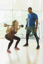 Personal trainer guiding woman doing barbell squats at gym - CAIF11823