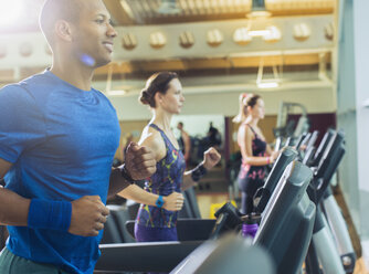 Smiling man running on treadmill at gym - CAIF11829