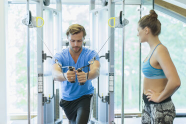 Personal trainer guiding man using cable exercise machine at gym - CAIF11836