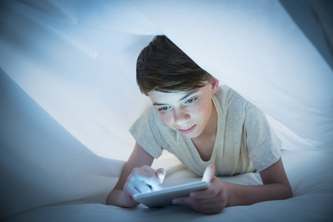 Junge benutzt digitales Tablet unter Laken, lizenzfreies Stockfoto