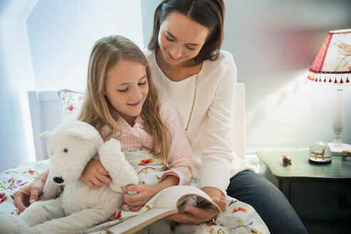 Mutter liest mit ihrer Tochter im Bett eine Gutenachtgeschichte - CAIF11863