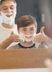 Father helping son pretending to shave in bathroom mirror - CAIF11867