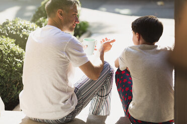 Vater mit Kaffee im Gespräch mit seinem Sohn auf der Treppe - CAIF11868