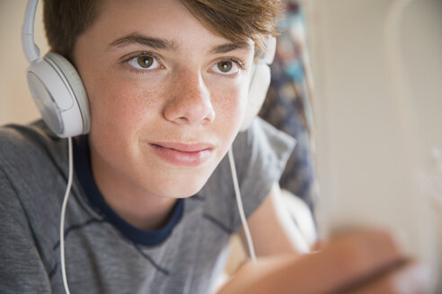 Nahaufnahme eines Jungen mit Kopfhörern, der auf einem digitalen Tablet Musik hört - CAIF11870