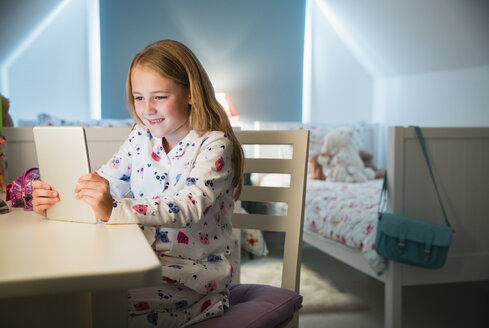 Mädchen im Pyjama mit digitalem Tablet am Schreibtisch im Schlafzimmer - CAIF11872