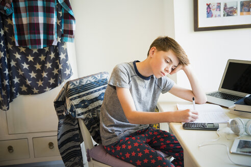 Gelangweilter Junge macht Mathe-Hausaufgaben am Schreibtisch im Schlafzimmer - CAIF11874