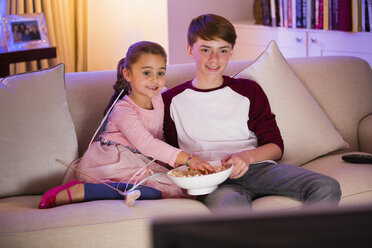 Bruder und Schwester essen Popcorn und sehen im Wohnzimmer fern - CAIF11877