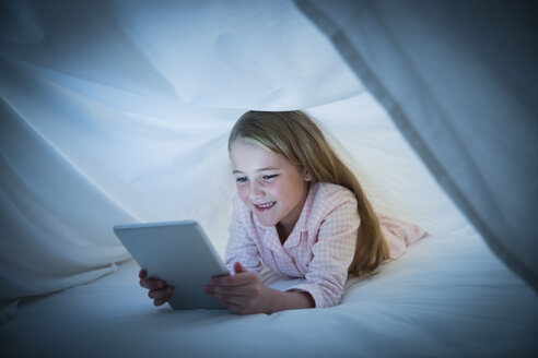 Lächelndes Mädchen mit digitalem Tablet unter dem Laken - CAIF11880